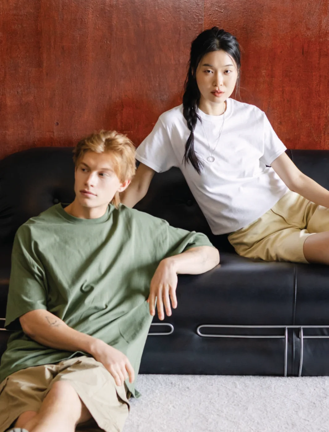 Two people in Gildan Ultra Cotton 2000 tees in military green and white, relaxing on a leather sofa