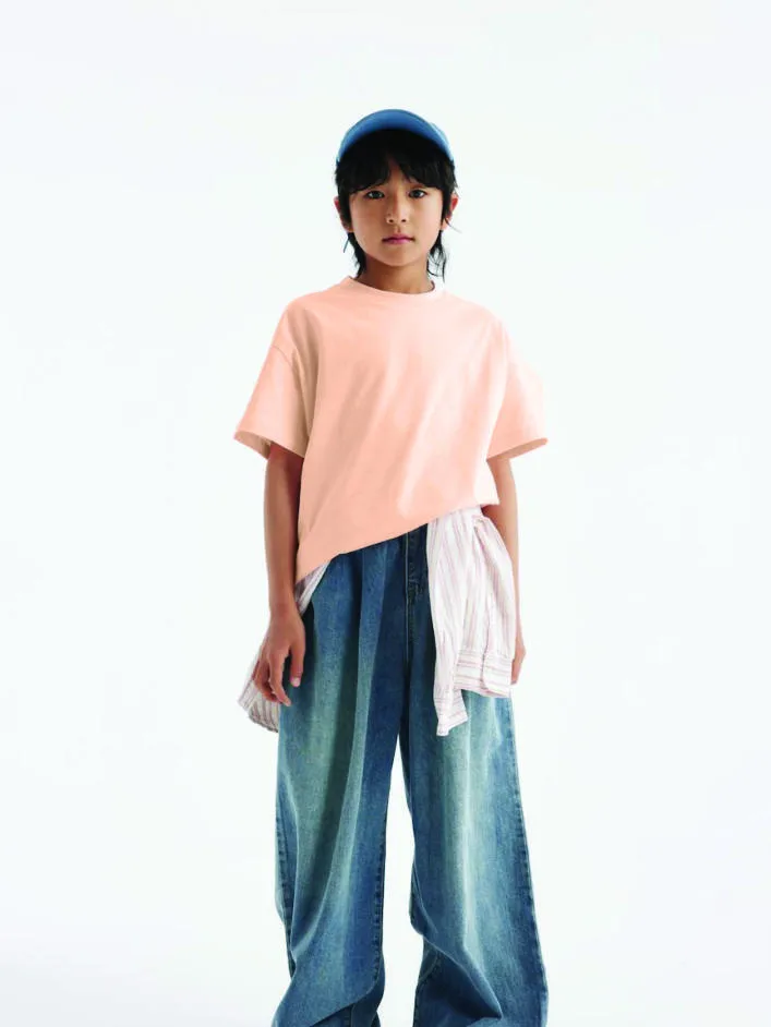 A child wearing a peach AG180B kids cotton tee with wide-leg jeans