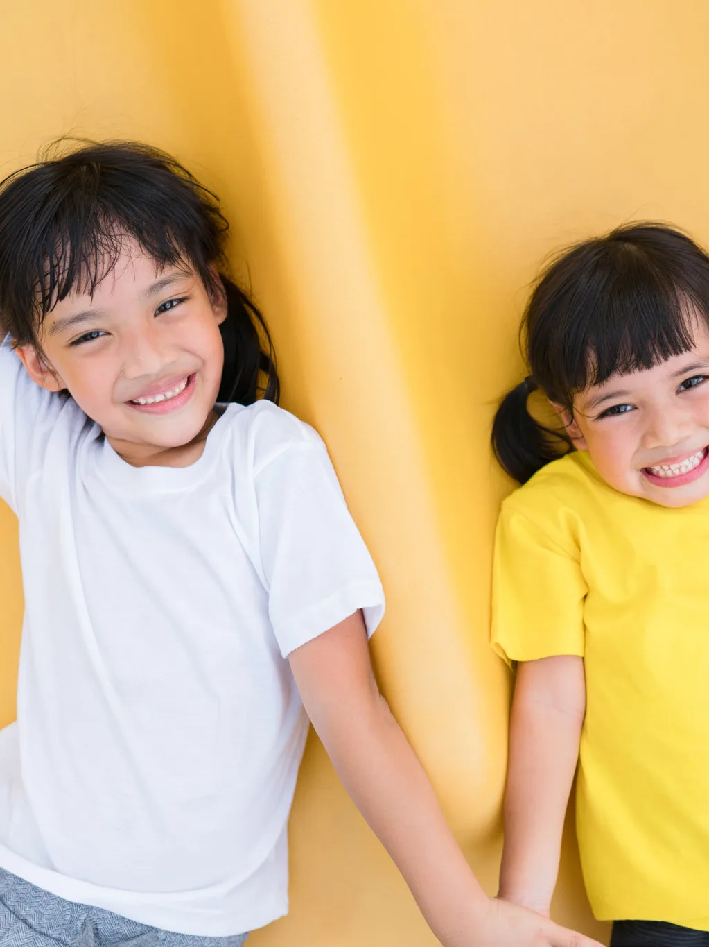 Two children lying on a yellow slide in Le'Fonse RCK01 kids tees, in white and yellow